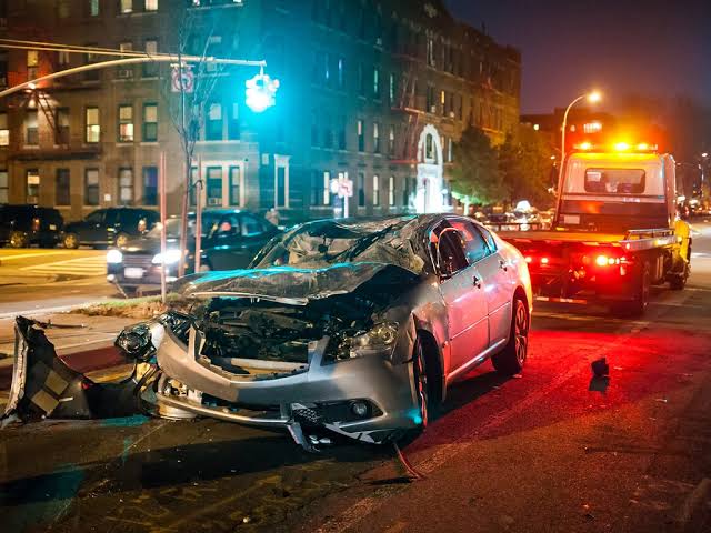 Sedán silver totalmente dañado siendo remolcado en Manhattan de noche